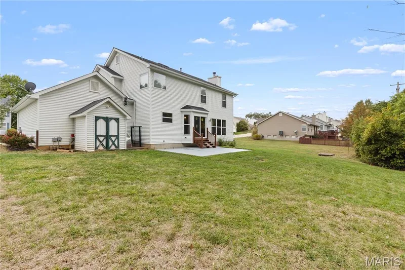 Two-story residence with white siding, rear concrete patio, attached exterior storage shed, and expansive yard — 838 Emerald Place Drive, St Charles, MO 63304