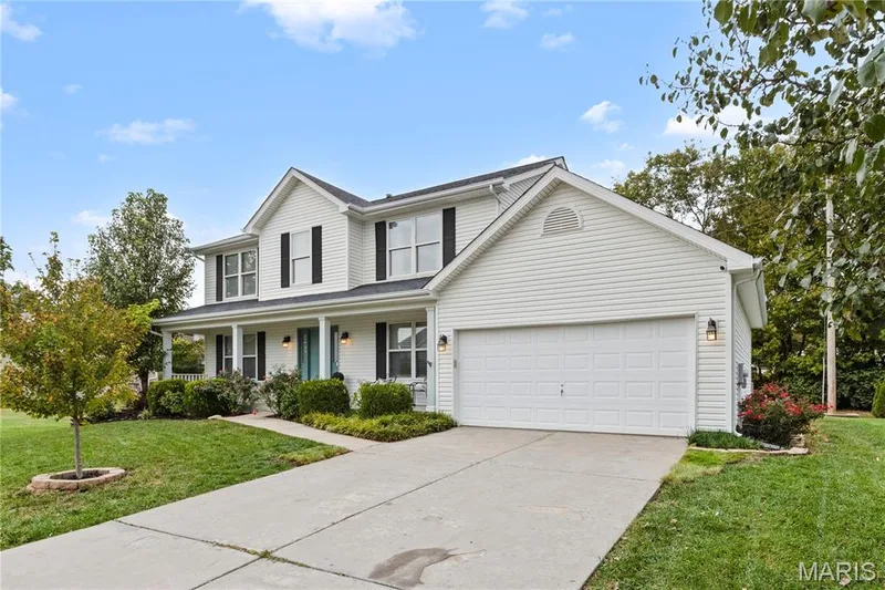 Two-story exterior featuring white vinyl siding, dark shutters, a front porch, and an attached two-car garage — 838 Emerald Place Drive, St Charles, MO 63304