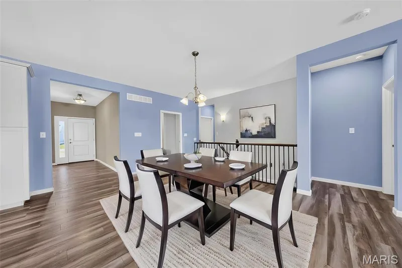 Open-concept dining area featuring wood-finish flooring, a contemporary chandelier, and a black metal railing — 622 Cruden Bay Court, Dardenne Prairie, MO 63368