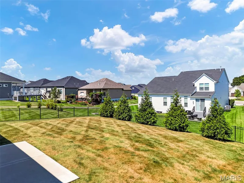 Expansive rear lawn with a black metal fence, concrete patio, and a row of evergreen trees — 622 Cruden Bay Court, Dardenne Prairie, MO 63368