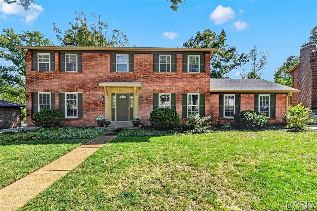Two-story colonial residence featuring a red brick exterior, symmetrical window placement, contrasting dark shutters, a covered front entryway, and a chimney — 15552 Chequer Drive, Chesterfield, MO 63017