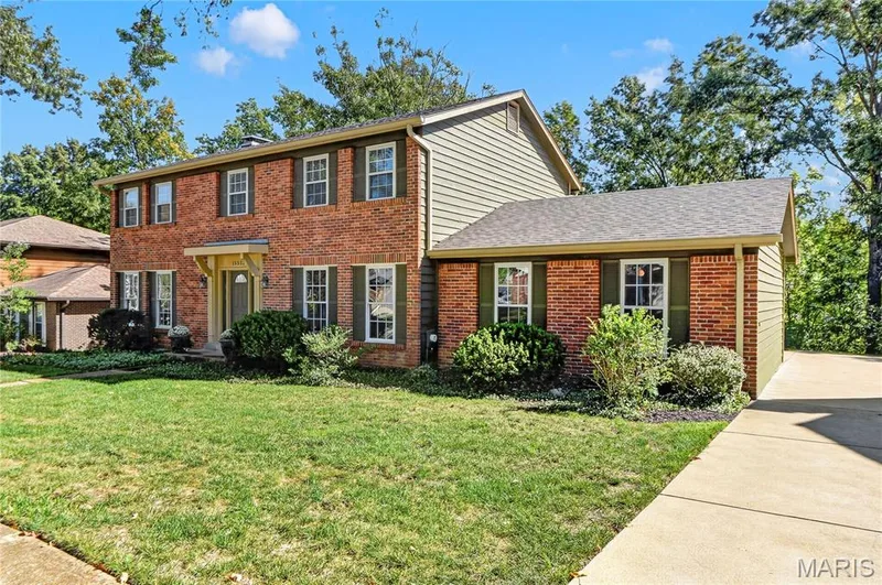 Two-story brick and horizontal siding exterior featuring a multi-pitched shingle roof, shuttered grid-pattern windows, and an attached concrete driveway — 15552 Chequer Drive, Chesterfield, MO 63017