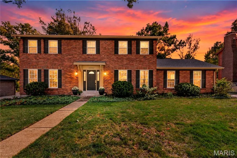 Two-story brick exterior featuring a covered entryway, decorative shutters, multi-pane windows, and a paved walkway — 15552 Chequer Drive, Chesterfield, MO 63017