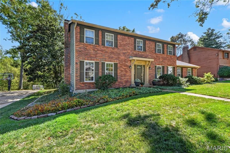 Two-story brick exterior featuring a covered entryway, decorative shutters, and stone-bordered landscaping — 15552 Chequer Drive, Chesterfield, MO 63017