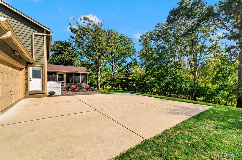 Expansive concrete patio featuring a dedicated screened-in enclosure, multi-paneled garage door, and mature tree-lined perimeter — 15552 Chequer Drive, Chesterfield, MO 63017