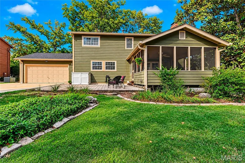 Exterior featuring horizontal siding, a screened-in porch, a paved stone patio, an attached garage, and stone-bordered landscaping beds — 15552 Chequer Drive, Chesterfield, MO 63017