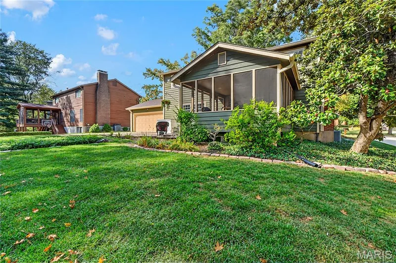 Screened-in porch featuring horizontal lap siding, expansive manicured lawn, stone-border garden beds, and mature landscaping — 15552 Chequer Drive, Chesterfield, MO 63017