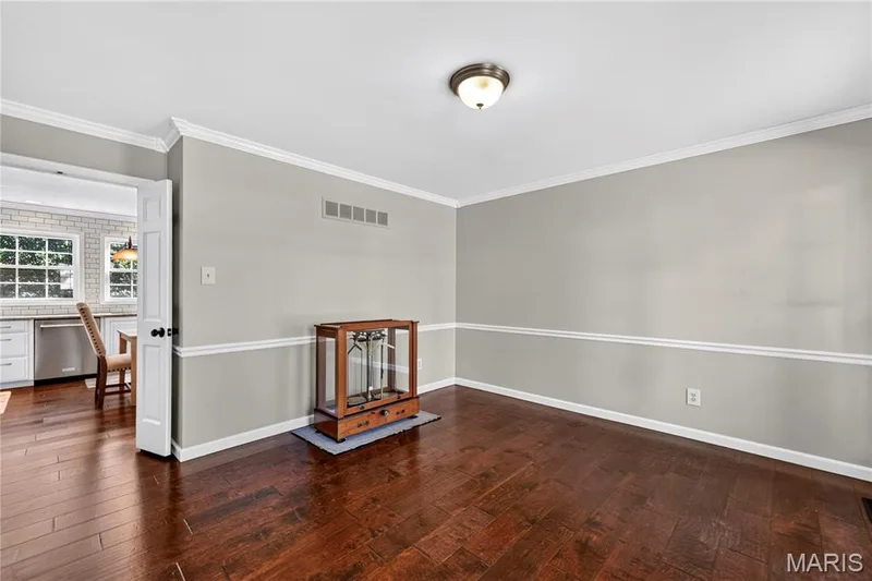 Interior room featuring dark wood-finish flooring, crisp white crown molding, chair rail trim, and a flush-mount ceiling light fixture — 15552 Chequer Drive, Chesterfield, MO 63017