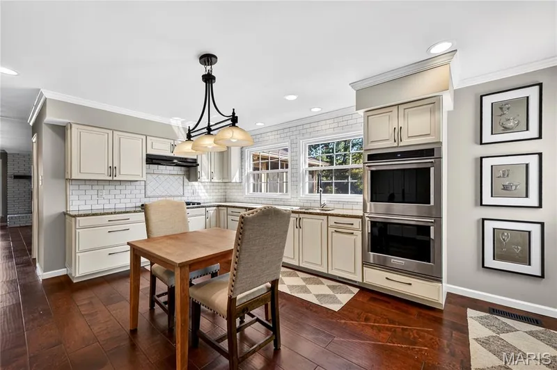 Kitchen featuring wood-finish flooring, white subway tile backsplash, stainless steel double wall ovens, multi-light chandelier, and light-toned cabinetry — 15552 Chequer Drive, Chesterfield, MO 63017