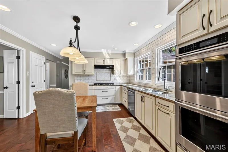 Kitchen featuring wood-finish flooring, cream-toned cabinetry, stainless steel double wall ovens, subway tile backsplash, and recessed lighting — 15552 Chequer Drive, Chesterfield, MO 63017
