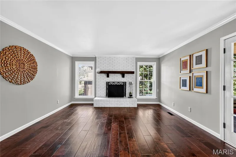 Living area featuring white painted brick fireplace, dark wood-finish flooring, crown molding, and dual windows — 15552 Chequer Drive, Chesterfield, MO 63017