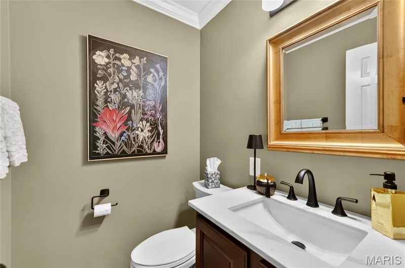 Vanity featuring a stone-composite countertop, undermount sink, and matte black widespread faucet, complemented by a framed mirror, crown molding, and dark-toned cabinetry — 15552 Chequer Drive, Chesterfield, MO 63017