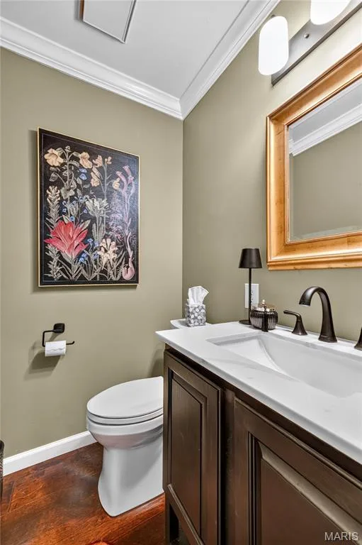 Wood-finish flooring, dark wood vanity with a white countertop and integrated sink, oil-rubbed bronze faucet, and crown molding — 15552 Chequer Drive, Chesterfield, MO 63017