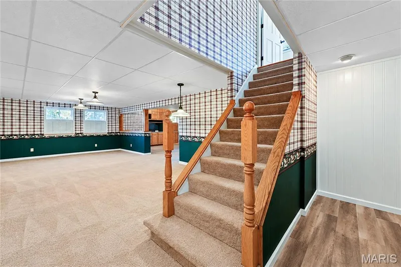 Finished interior space featuring carpeted flooring, wood-toned handrails with turned balusters, suspended ceiling tiles, and built-in wood cabinetry — 15552 Chequer Drive, Chesterfield, MO 63017