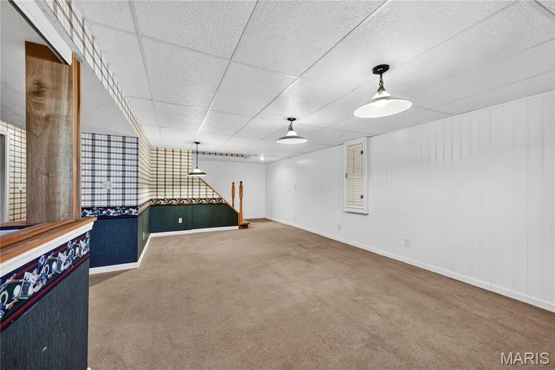 Finished interior space featuring carpeted flooring, white vertical wall paneling, a drop ceiling, and three pendant light fixtures — 15552 Chequer Drive, Chesterfield, MO 63017