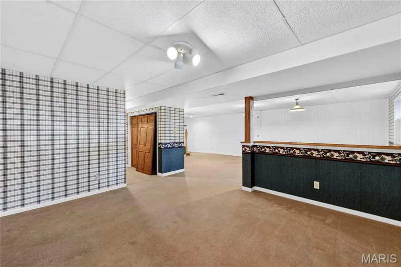 Open interior space featuring a drop ceiling, wall-to-wall carpeting, wood-paneled closet doors, and half-wall partitioning with chair rail detailing — 15552 Chequer Drive, Chesterfield, MO 63017