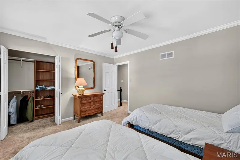 Neutral-toned room featuring a built-in closet with shelving, crown molding, wall-to-wall carpeting, and a ceiling fan with integrated light fixture — 15552 Chequer Drive, Chesterfield, MO 63017