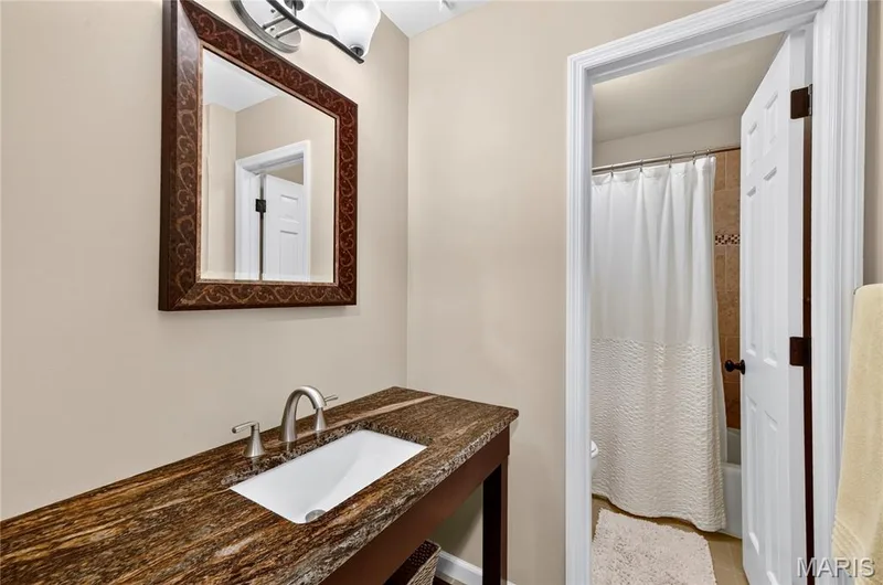 Vanity featuring stone-finish countertop, under-mount basin, and metallic faucet, complemented by a decorative wall-mounted mirror and two-light fixture — 15552 Chequer Drive, Chesterfield, MO 63017