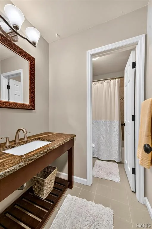Console vanity featuring a stone countertop, integrated rectangular sink, open slatted lower shelf, and a three-light wall fixture — 15552 Chequer Drive, Chesterfield, MO 63017
