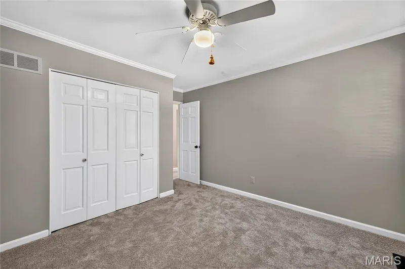 Neutral-toned interior featuring wall-to-wall carpeting, ceiling fan with light fixture, and floor-to-ceiling bi-fold closet doors — 15552 Chequer Drive, Chesterfield, MO 63017