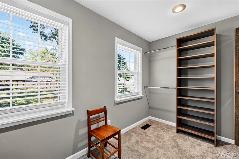 Built-in floor-to-ceiling shelving, dual wall-mounted metal clothing rods, two windows with horizontal blinds, neutral wall finish, and carpet flooring — 15552 Chequer Drive, Chesterfield, MO 63017