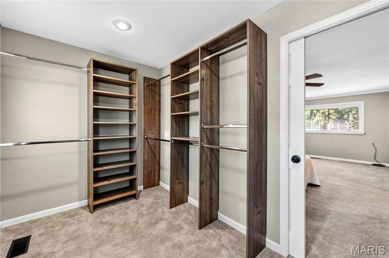 Luxurious walk-in closet featuring custom wood-finish cabinetry with multiple shelving sections, a dedicated shoe rack with individual slots, and mirrored sliding doors — 15552 Chequer Drive, Chesterfield, MO 63017