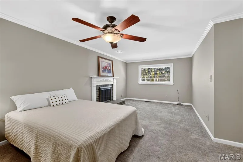 Room featuring a wood-burning fireplace with a decorative mantel, carpeted flooring, crown molding, and a central ceiling fan with integrated lighting — 15552 Chequer Drive, Chesterfield, MO 63017