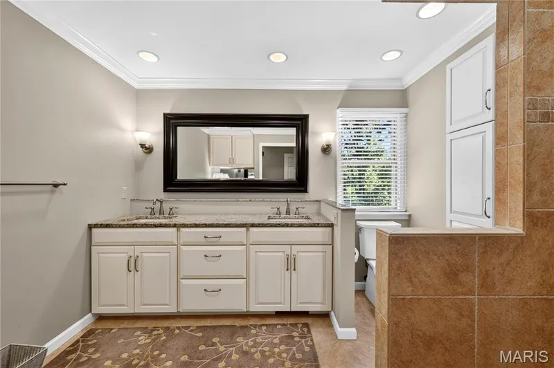 Dual-sink vanity with stone countertop, recessed lighting, crown molding, built-in cabinetry, and tile-surround partitions — 15552 Chequer Drive, Chesterfield, MO 63017