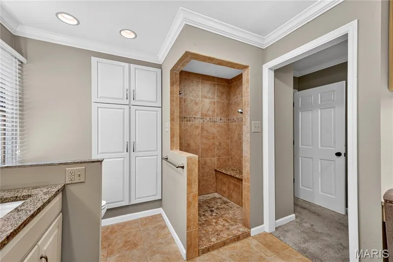 Bathroom featuring a walk-in shower with stone tile surround, built-in shower bench, and decorative tile inlay — 15552 Chequer Drive, Chesterfield, MO 63017