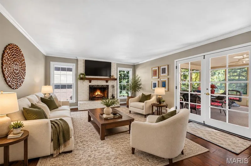 Living room featuring white painted brick fireplace, wooden mantel, crown molding, wood-finish flooring, and multi-pane glass double doors — 15552 Chequer Drive, Chesterfield, MO 63017