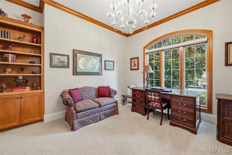 Built-in wooden shelving with lower cabinetry, arched window with wood trim, crown molding, and a multi-tiered chandelier — 112 Castlewood Estates Drive, O'Fallon, MO 63368