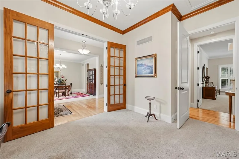 Office featuring glass-paned French doors, custom wood crown molding, a central multi-arm chandelier, and wall-to-wall carpeting — 112 Castlewood Estates Drive, O'Fallon, MO 63368