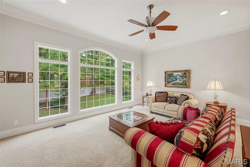 Great Room featuring arched windows with grid detailing, crown molding, neutral carpeting, and a ceiling fan with integrated lighting — 112 Castlewood Estates Drive, O'Fallon, MO 63368