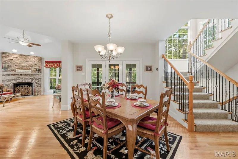 Exposed brick fireplace, wood-finish flooring, multi-light chandelier, French doors, and staircase featuring a wood handrail with metal balusters — 112 Castlewood Estates Drive, O'Fallon, MO 63368