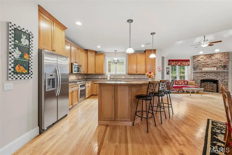 Kitchen featuring light wood cabinetry, stone countertops, stainless steel appliances, pendant lighting, and wood-finish flooring — 112 Castlewood Estates Drive, O'Fallon, MO 63368