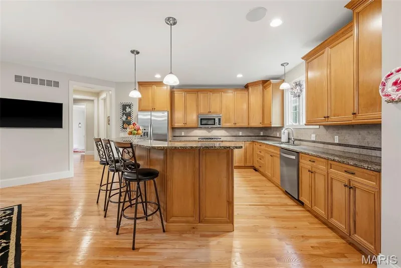 Kitchen featuring wood cabinetry, stone countertops, stainless steel appliances, wood-finish flooring, and pendant lighting — 112 Castlewood Estates Drive, O'Fallon, MO 63368