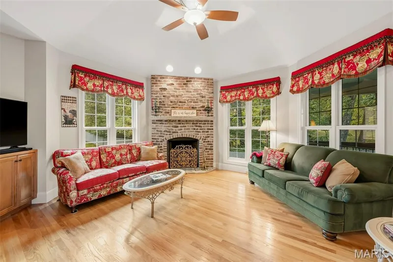 Hearth Room with Vaulted ceiling featuring a central paddle fan, wood-finish flooring, and a floor-to-ceiling brick fireplace with an arched firebox — 112 Castlewood Estates Drive, O'Fallon, MO 63368