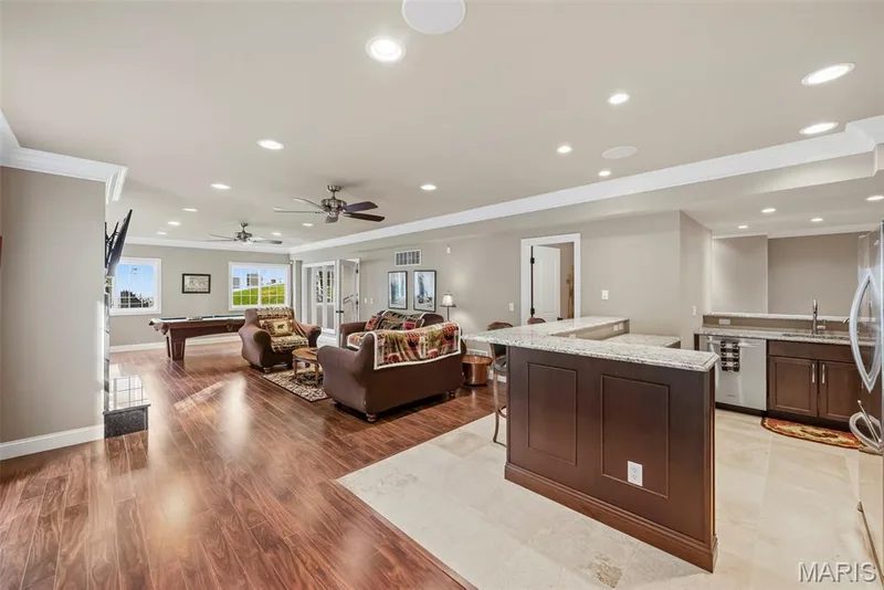 Finished Lower Level featuring wood-finish flooring, stone-tile flooring in the kitchen area, a raised breakfast bar with stone countertop, dark wood cabinetry, and recessed lighting — 112 Castlewood Estates Drive, O'Fallon, MO 63368