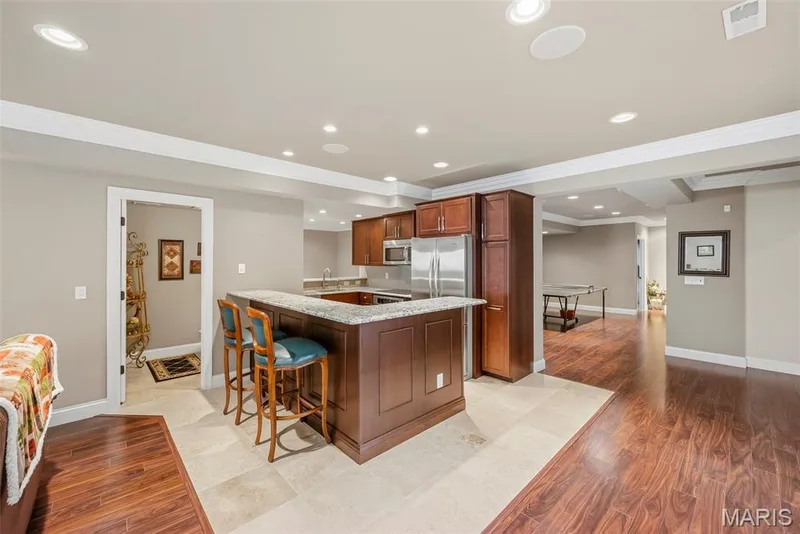 Lower Level Kitchen area featuring stained wood cabinetry, stone-finish countertops, recessed lighting, and a combination of stone-tile and wood-finish flooring — 112 Castlewood Estates Drive, O'Fallon, MO 63368