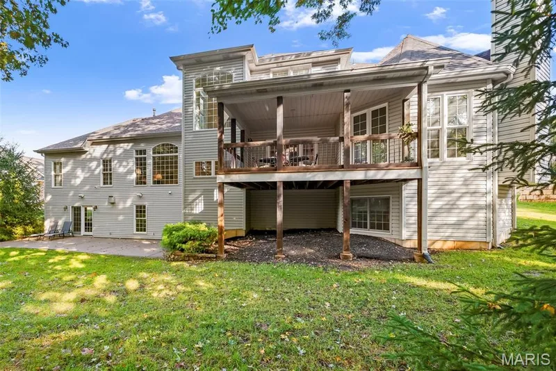 Rear exterior featuring vinyl siding, an elevated wood-framed covered deck, a lower-level concrete patio, and grid-pattern windows — 112 Castlewood Estates Drive, O'Fallon, MO 63368