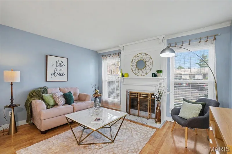 Hardwood flooring, white crown molding, a decorative fireplace with a gold-toned screen, and large windows with privacy blinds — 81 Schooner Lane #1, Lake St. Louis, MO 63367