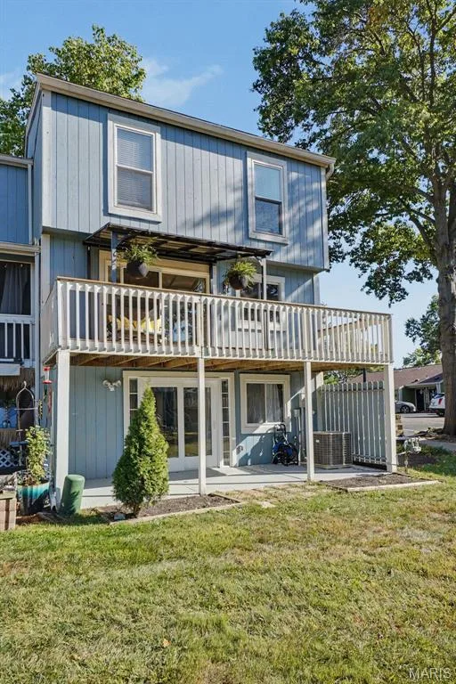 Two-story exterior with vertical siding, a second-story balcony with wood railing, a ground-level patio, and French patio doors — 81 Schooner Lane #1, Lake St. Louis, MO 63367