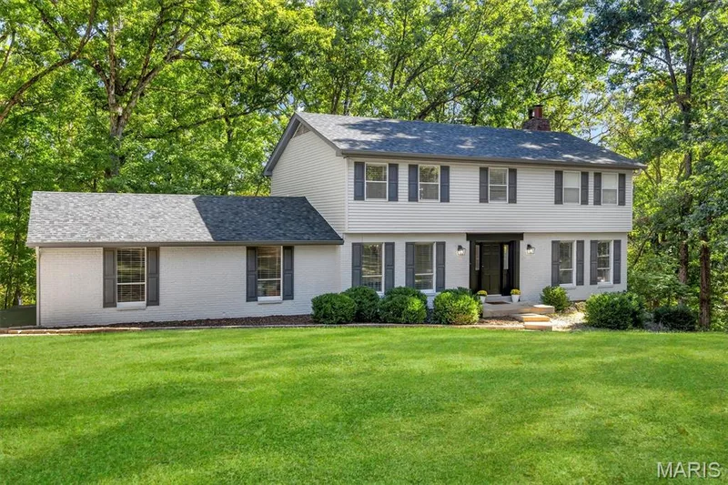 Two-story exterior featuring painted brick and siding, dark shutter accents, architectural shingle roofing, and a manicured lawn framed by mature trees — 1444 Eagle Ridge Road, Wildwood, MO 63038