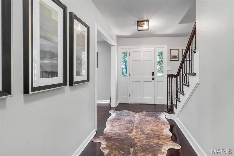 Entryway featuring white six-panel door with sidelights, dark-stained wood-finish flooring, staircase with dark wood handrail and metal balusters, and square flush-mount ceiling lighting — 1444 Eagle Ridge Road, Wildwood, MO 63038