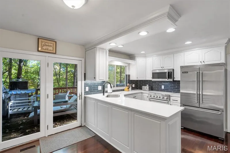 Kitchen featuring white cabinetry, quartz countertops, a dark-toned tile backsplash, stainless steel appliances, and wood-finish flooring — 1444 Eagle Ridge Road, Wildwood, MO 63038