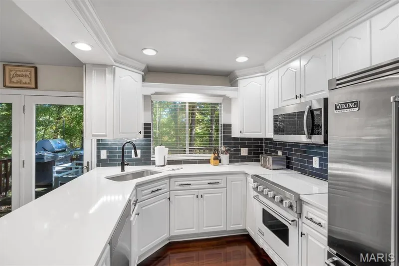 Kitchen featuring white cabinetry, solid-surface countertops, dark subway-tile backsplash, stainless steel Viking appliances, and wood-finish flooring — 1444 Eagle Ridge Road, Wildwood, MO 63038