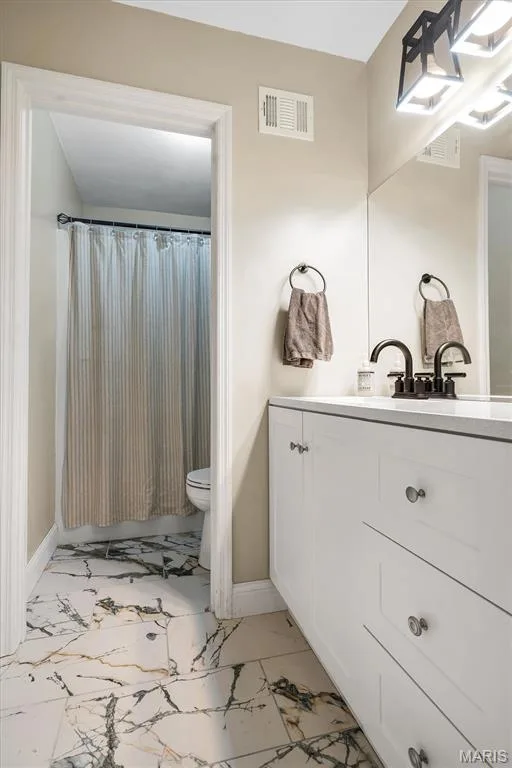 White vanity cabinet with light-toned countertop, dark-finish faucet, wall-spanning mirror, and high-contrast veined tile flooring — 1444 Eagle Ridge Road, Wildwood, MO 63038
