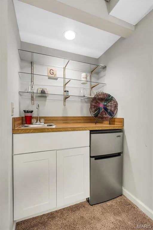 Wet bar area featuring white shaker-style cabinetry, wood-finish countertop, stainless steel sink with faucet, compact refrigerator, and adjustable glass shelving — 1444 Eagle Ridge Road, Wildwood, MO 63038