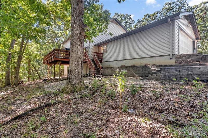 Exterior featuring horizontal siding, an elevated wood deck with stairs, a stone-block retaining wall, and an attached two-car garage — 1444 Eagle Ridge Road, Wildwood, MO 63038
