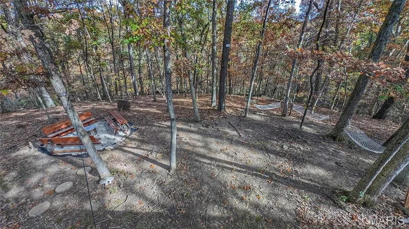 Wooded lot featuring a stone-bordered fire pit with built-in wooden bench seating, natural terrain, and mature deciduous trees — 1444 Eagle Ridge Road, Wildwood, MO 63038